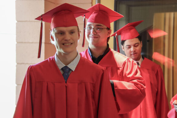 Three students stand in line with graduation gowns on