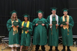 five graduates standing and smiling with their diplomas 