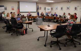 The Education Professional Standards Board sits around a collection of tables and listens to Robin Fields Kinney