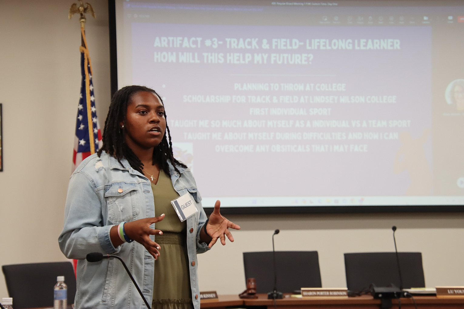 Navaeh Acklin talking in a board room with her presentation showing on a screen behind her, reading Artifact #3, Track and Field, Lifelong Learner. How will this help my future?