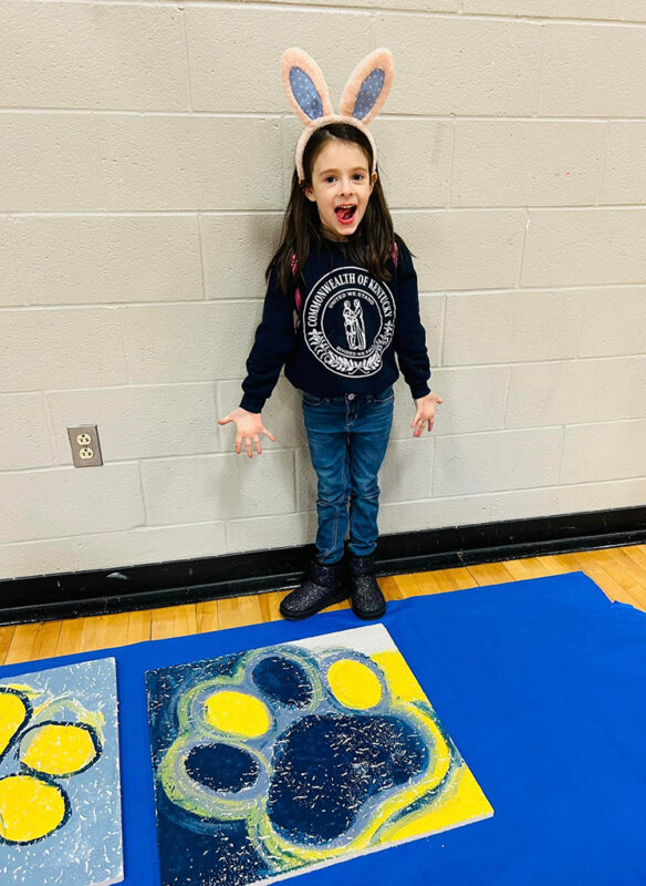 A girl stands over an animal's paw that she painted on a canvas
