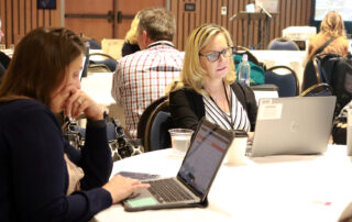 Two women sit while working on laptops