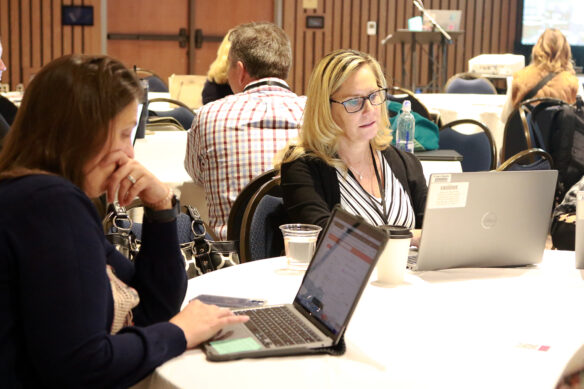 Two women sit while working on laptops