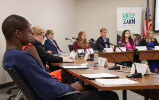 Members of KDE's Commissioner's Student Advisory Council sit around tables, listening to a presentation.