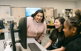 A woman and two students look at a computer monitor