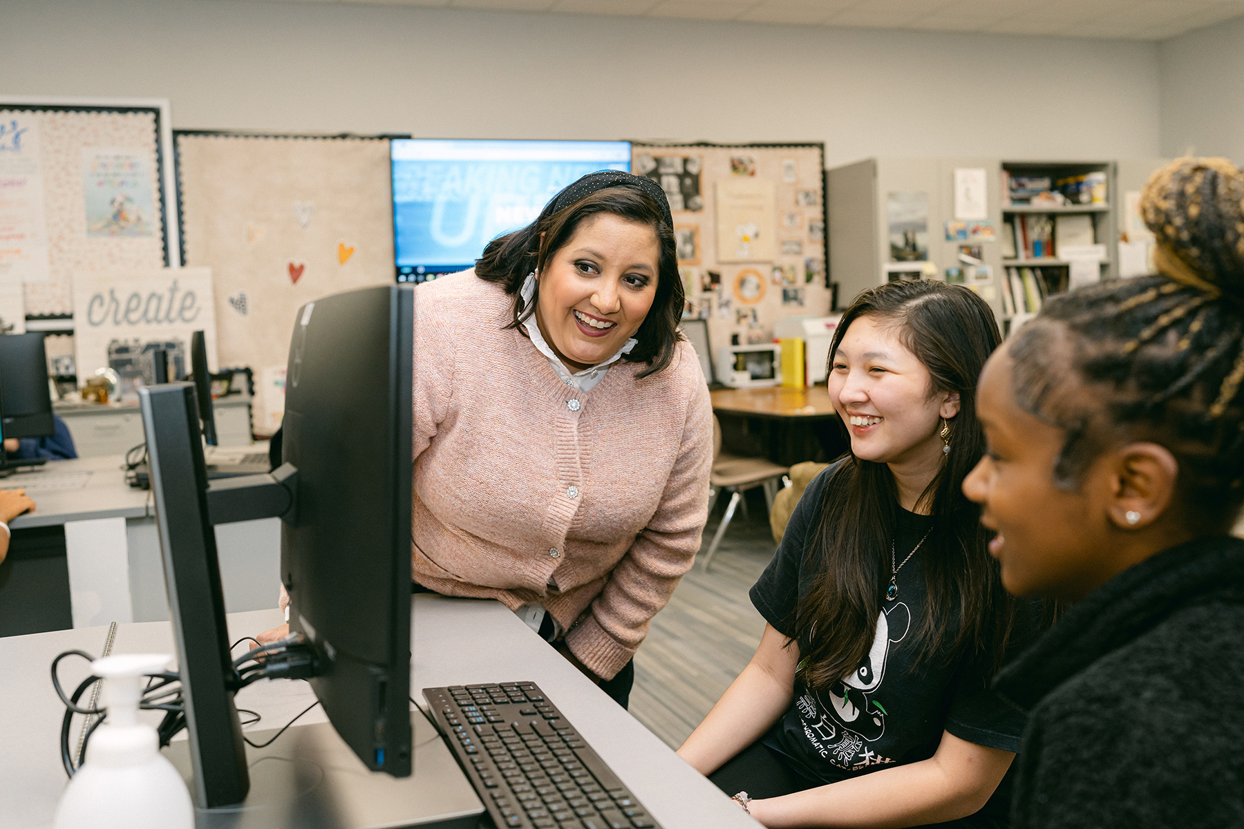 A woman and two students look at a computer monitor