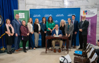 A group of people, including Gov. Andy Beshear, sit around him at a table as he signs a proclamation