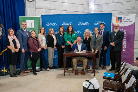 A group of people, including Gov. Andy Beshear, sit around him at a table as he signs a proclamation