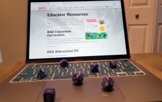 A computer with multiple die on the keyboard and the Dungeons and Dragons Educator Resources webpage