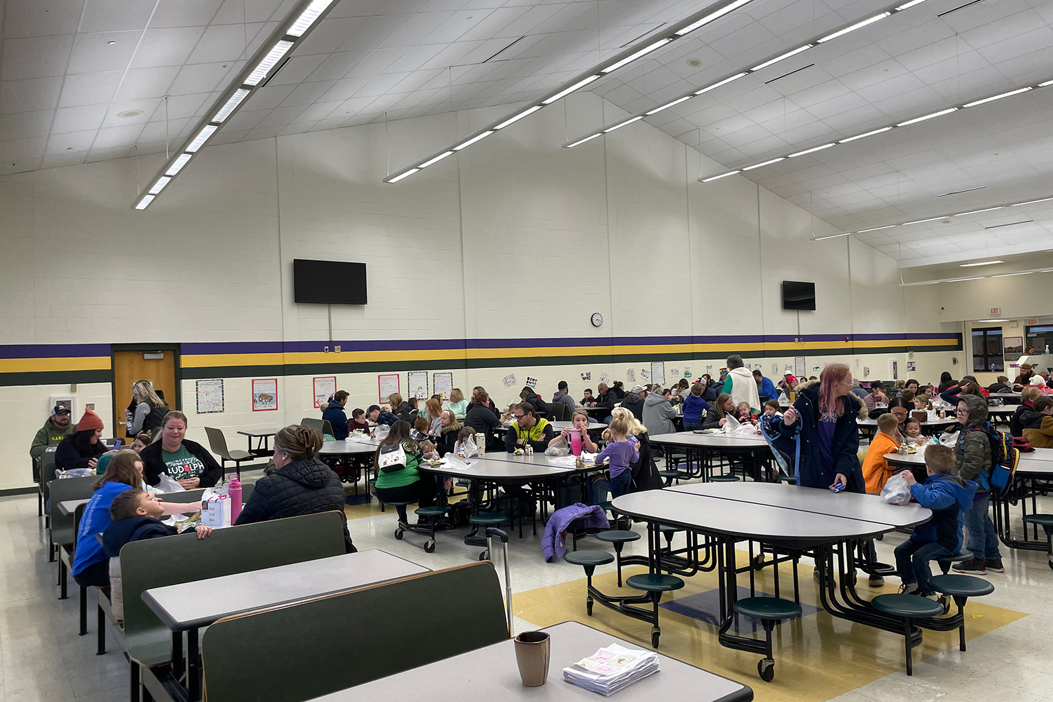 A group of people sit at various tables inside a gymnasium